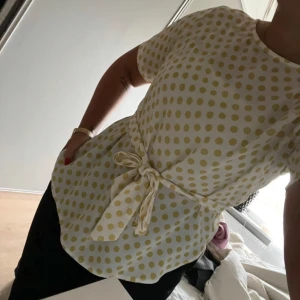 Vit och gul prickig blus med knytband - Säljer en söt vit blus med gula prickar och knytband i midjan. Blusen har korta ärmar och en rund halsringning. Storlek S,normal i storlek. I bra skick. 
