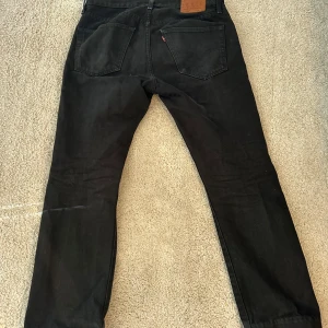 Svarta Levis 501 jeans - Säljer ett par klassiska svarta Levis 501 jeans. De har en knappgylf och femficksdesign. Perfekta för en stilren look. Passar till många olika outfits!