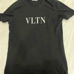 Valentino t shirt - Snygg svart t-shirt från Valentino med det ikoniska VLTN-trycket i vitt på bröstet. Perfekt för en stilren och modern look. T-shirten har en klassisk passform och korta ärmar. Storlek M men passar S. Skicket är ca 7/10 då den är rätt trött vid trycket