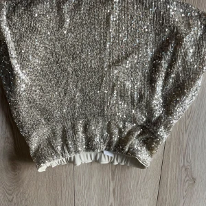 Glittrig kjol från Lindex - Snygg glittrig kjol från Lindex i en skimrande guldfärg . Perfekt för att sticka ut på festen. Kjolen har en elastisk midja för bekväm passform.🩷