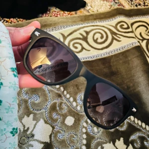 Svarta solglasögon med mönstrade skalmar från Unofficial  - Snygga svarta solglasögon med mörka linser och unika mönstrade skalmar. Perfekta för en stilren look. Passar både till vardag och speciella tillfällen.