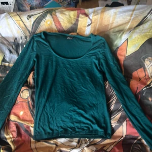Grön långärmad topp från Gina Tricot - Säljer en stilren grön långärmad topp från Gina Tricot. Är utvikta längs ned vid armen. Har en fläck som borde gå bort i tvätten 💗