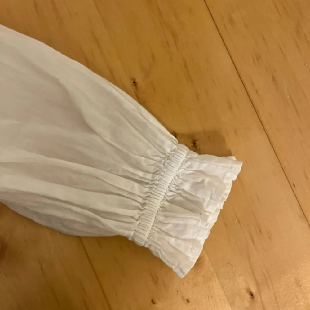Säljer en söt vit blus från Lindex med spetsdetaljer och volanger framtill. Blusen har långa ärmar med elastiska muddar och en smockad rygg för en bekväm passform. Den är använd endast en gång🌼. Puserot.