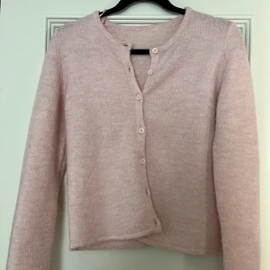 Ljusrosa kofta med knappar - Säljer en söt ljusrosa kofta med knappar framtill. Den har en rund halsringning och långa ärmar, perfekt för kyligare dagar. Koftan är mjuk och bekväm att bära.