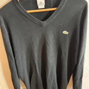 Svart tröja från Lacoste - Säljer en stilren svart tröja från Lacoste med v-ringning och det klassiska krokodilmärket broderat på bröstet. Tröjan har långa ärmar och är perfekt för en avslappnad men ändå elegant look. 