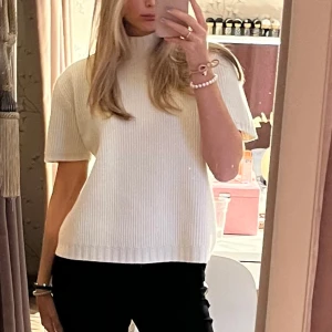 Vit ribbad tröja - Säljer en stilren vit ribbad tröja med korta ärmar och hög krage. Perfekt för en elegant och avslappnad look. Passar bra till både jeans och kjol.