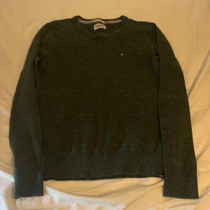 Grön tröja från Hilfiger Denim - Säljer en snygg grön tröja från Hilfiger Denim med v-ringning och diskret logga på bröstet.