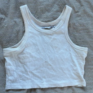 Vit ribbad linnetopp från 157 - Säljer en stilren vit ribbad linnetopp från lager 157. Perfekt för varma dagar med sin ärmlösa design och croppade längd. Enkel och snygg att matcha med olika outfits.