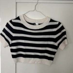 Randig croppad topp från H&M - Säljer en snygg, stickad och croppad topp från H&M i svart och vitt. Toppen har korta ärmar och är ribbad vid hals och nederkant. 