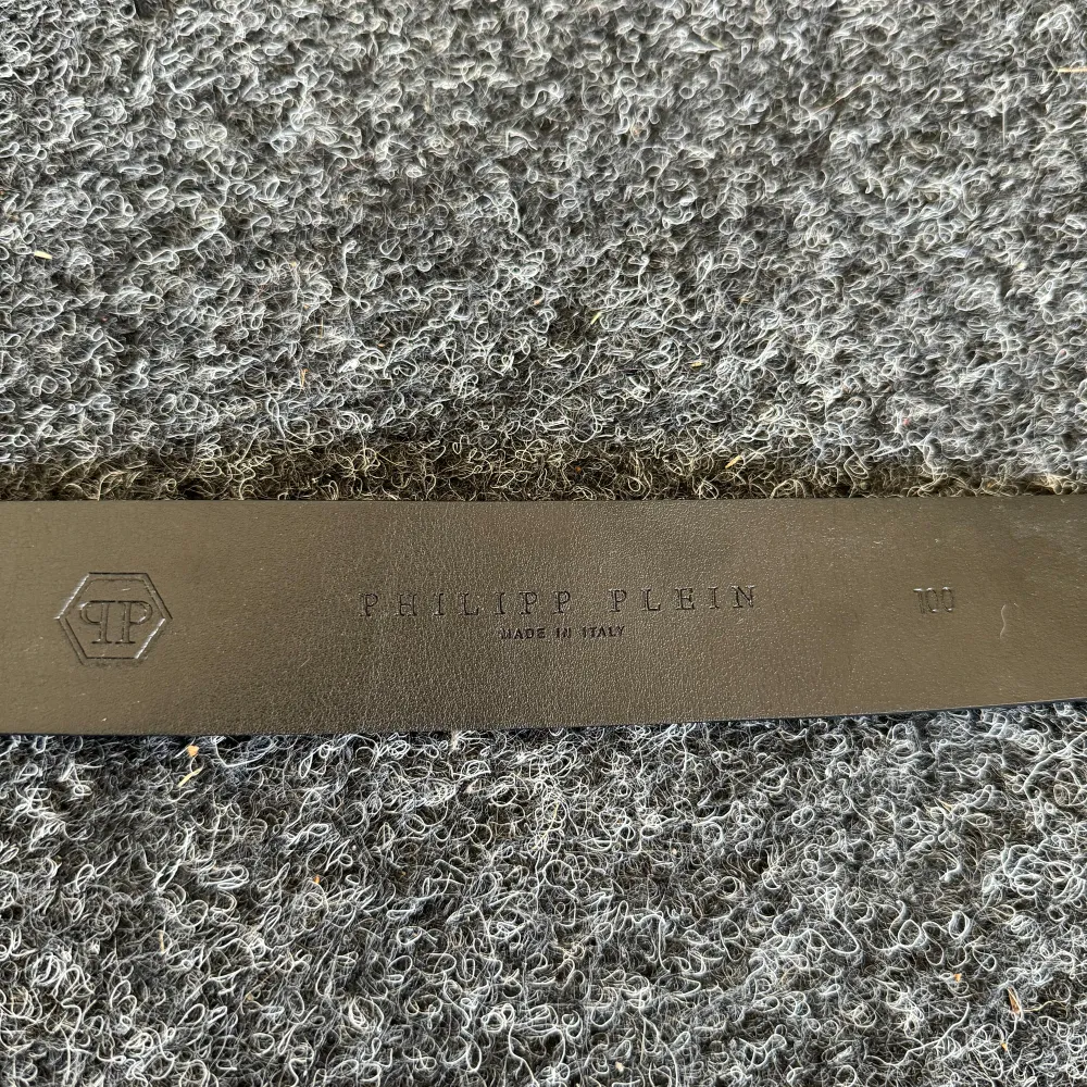 Snyggt svart skärp från Philipp Plein med en iögonfallande silverfärgad spänne. Tillverkat i Italien och har en exklusiv känsla med präglad logotyp och detaljer. Perfekt för att ge en lyxig touch till din outfit.. Asusteet.
