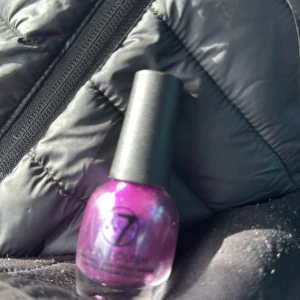 Lila nagellack från W7 - Snyggt lila nagellack från W7 med en skimrande finish. Perfekt för att ge dina naglar en färgstark och glittrig look. Kommer i en praktisk flaska med en lättanvänd borste för enkel applicering.