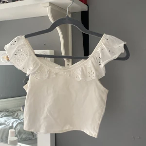 Vit broderad topp från H&M - Säljer en söt vit topp från H&M med broderade detaljer och volangärmar. Toppen är croppad och har  fina spetsmönster. Perfekt för varma sommardagar! 💘 jag har aldrig använt ❤️