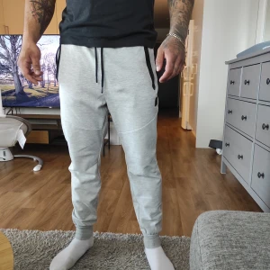 Grå mjukisbyxor med snörning - Säljer ett par bekväma grå mjukisbyxor med snörning i midjan. Byxorna har en normal passform och är perfekta för en avslappnad stil. De har svarta detaljer vid fickorna och är tillverkade i ett mjukt material. Från Stadium.