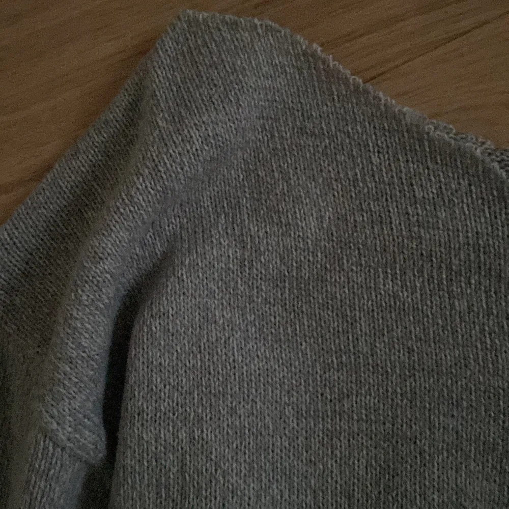 Säljer en mysig grå stickad tröja med långa ärmar. Perfekt för kyliga dagar med sin mjuka och bekväma passform. Tröjan har ribbade muddar vid ärmslut och nederkant.. Neuletakit & Villapaidat.