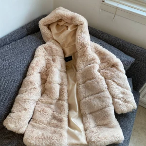 Beige pälsjacka med huva Garoff - Säljer en supermjuk och fluffig beige pälsjacka med huva. Jackan har en oversized passform och är perfekt för kyliga dagar. Den är långärmad och har en mysig känsla som gör den till ett måste i garderoben.