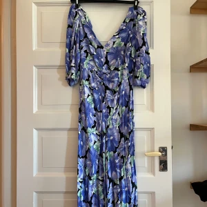 Blommig klänning - Blå- och grön blommig klänning med lite puffärmar, dragkedja bak. Perfekt till examensfirande eller andra somriga tillställningar!!