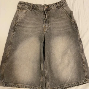 Grå jeansshorts från Bershka - Säljer ett par grå jeansshorts från Bershka. De har en klassisk femficksdesign och en knappgylf. Perfekta för en avslappnad stil. Tillverkade i Turkiet.