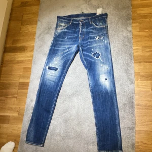 Blå jeans från Dsquared2 - Säljer ett par blå jeans från Dsquared2 med slitna detaljer och hål för en trendig look. Jeansen har en knappgylf och klassisk femficksdesign. Äkta och kvitto finns med