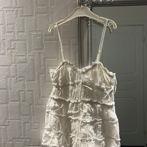 Vit topp  - Charmig vit topp med   smala axelband. Perfekt för sommarens varma dagar. Den har en söt knytning framtill och en luftig design, toppen är klippt och var tidigare en klänning