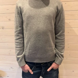 Grå stickad tröja - Säljer en stilren grå stickad tröja med rund hals och ribbade muddar. Perfekt för kyligare dagar och enkel att matcha med olika outfits.