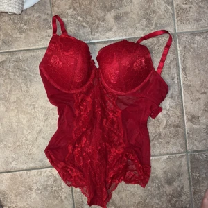 Röd spetskorsett från H&M - Snygg röd korsett från H&M med spetsdetaljer och justerbara axelband. Modellen har vadderade kupor, hakknäppning bak och transparent mesh i sidorna. Perfekt för dig som vill ha en statement piece med romantisk vibe.