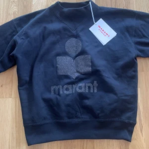Svart sweatshirt från Isabel marant  - Svart sweatshirt från Isabel marant med glittrigt tryck. Köpt från bergdorf goodman. Tröjan har använts ca 2 gånger. Prislappen/äkthetsbevis finns inte kvar på tröjan, men man får med på sidan. I övrigt är tröjan i ett mycket fint skick och i storlek xs/34.