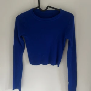 Blå croppad ribbad tröja - Säljer en blå croppad tröja med ribbad struktur och långa ärmar. Perfekt för dig som gillar en enkel men trendig stil. Snygg att matcha med både jeans och kjol.