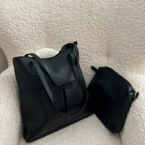 Svart axelväska med tillhörande necessär - Stilren svart axelväska i slätt material med matchande necessär. Väskan har dubbla handtag och enkel design utan synliga detaljer. Perfekt för att bära med sig det viktigaste till vardags.