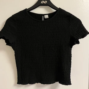 Svart smockad topp - En svart smockad topp från H&M Divided i storlek S. Materialet är stretchigt men är lite mindre i storleken ä vanligt, enligt mig. 