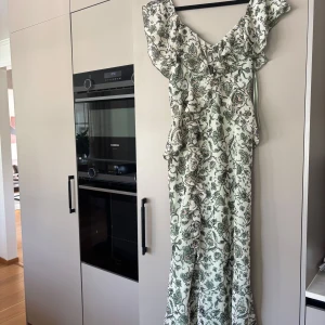 Lång blommig klänning med volang - Superfin långklänning i ljusgrönt och vitt med blommigt mönster och volangdetaljer längs axlar och framstycke. Klänningen har omlottkänsla och är ärmlös med v-ringning. Perfekt för sommarens alla tillfällen! Helt slutsåld 🫶🏼