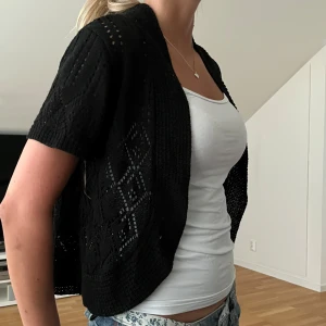 Svart stickad bolero  - Säljer en svart stickad kofta från Notations i storlek S. Koftan har korta ärmar och ett öppet, luftigt mönster som ger en lätt och somrig känsla. Perfekt att slänga över ett linne eller t-shirt.