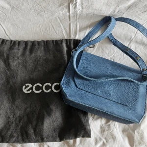 Eyota Blå axelväska från ECCO - Säljer en stilren blå Eyota axelväska från ECCO i äkta skinn. Väskan har justerbar axelrem, magnetlås och ett enkelt, modernt utseende. Perfekt för dig som vill ha en praktisk och snygg accessoar till vardagen.