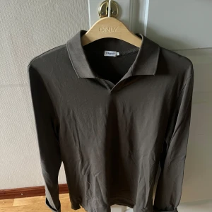 Brun långärmad pikétröja Filippa K - Snygg brun långärmad pikétröja från Filippa K med klassisk krage. Tröjan har en stilren, minimalistisk look som passar perfekt till jeans eller chinos. Enkel att matcha och riktigt skön att bära.