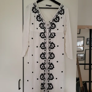 Vit klänning med broderi, Boohoo -  vit klänning från Boohoo med svarta broderade blommor framtill. Klänningen har v-ringning, långa ärmar och är tillverkad i ett tunt, lätt tyg. 