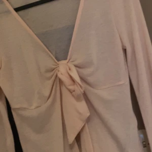 Ljusrosa omlottopp med knyt - Supersöt ljusrosa omlottopp med lång ärm och knyt framtill. Djup v-ringning och mjukt, tunt tyg som känns skönt mot huden. Perfekt för dig som gillar  feminin stil. 