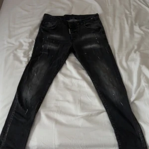 Svarta Dsquared2 jeans med slitningar - Snygga svarta jeans från Dsquared2 med coola slitningar och blekta detaljer. Klassisk femficksmodell med Dsquared2-logga vid gylfen och bak på linningen. Jeansen har en smal passform och är tillverkade i stretchig denim för extra komfort.