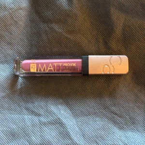 Matt flytande läppstift i lila nyans - Matt flytande läppstift från Pro Ink i färgen 010 I Choose Passion. Kommer i en genomskinlig tub med silvrigt lock. Läppstiftet har en intensiv lila ton och ger en matt finish.