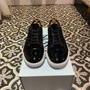 Lanvin skor - Snygga svarta sneakers från Lanvin med vit sula. Ovandelen är i blankt skinn och mocka, med rund tå och svarta skosnören. Klassisk och stilren modell som passar till det mesta. Kommer med box och originalpåse från Lanvin.