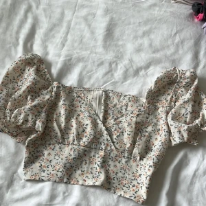 Blommig kortkjol med volang - Supersöt kortkjol i ljusbeige med små blommor i orange och grått. Kjolen har volangdetaljer och resår i midjan för en bekväm passform. Perfekt för dig som gillar romantisk och somrig stil.