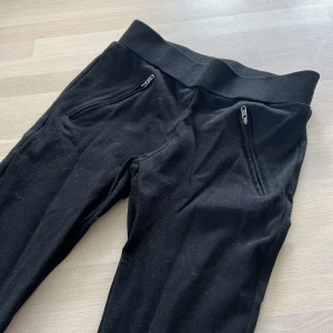 Svarta mjukisbyxor från Vila XS - Svarta mjukisbyxor från Vila i storlek XS. Byxorna har bred resår i midjan, två dragkedjefickor fram och raka ben. Sköna och enkla att matcha till olika outfits. Perfekta för chill dagar eller när du vill vara bekväm.
