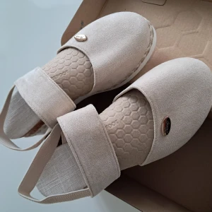 Beige sandaler med kilklack från Hong str 38 - Snygga beige sandaler med breda band och elastisk hälrem. Skorna har en vit plattformsula och kilklack med flätad detalj. Ovandelen har ett diskret hexagonmönster och en liten metallbricka med märkesnamnet.