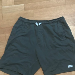 Mörkgröna shorts med snörning från 157 - Mörkgröna shorts från 157 med elastisk midja och vit snörning. Två sidofickor fram och en bakficka. Tillverkade i mjuk bomull, perfekta för avslappnade dagar.