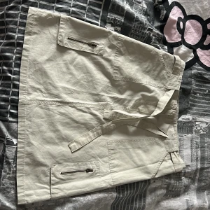 Beige utilitykjol från H&M med fickor - Snygg beige utilitykjol från H&M med flera stora fickor, dragkedjor och knytband i midjan. Kjolen är kort och har en rak passform. 