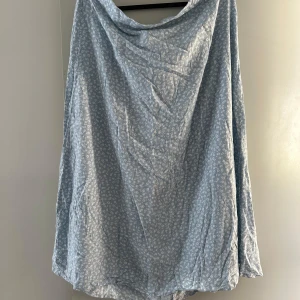 Ljusblå blommig kjol från Monki - Säljer en ljusblå kjol från Monki i storlek XL. Kjolen har ett diskret blommigt mönster och är tillverkad i ett mjukt och lätt material, perfekt för varmare dagar. Avslappnad passform, resår i midjan