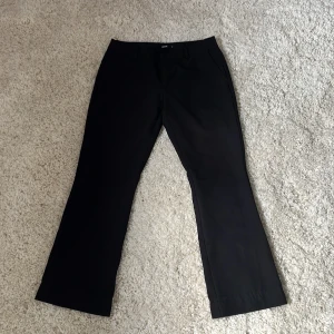 Svarta kostymbyxor från BikBok - Svarta kostymbyxor från BikBok i klassisk modell med utsvängda ben och diskreta fickor fram. Byxorna har hällor för bälte och stängs med knapp och dragkedja. Perfekta för en clean och stilren look.