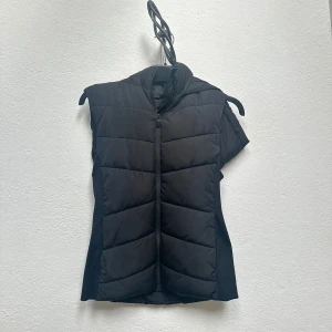 Svart dunväst med huva från Zara - Säljer en svart dunväst från Zara med dragkedja och stor huva. Västen har en stilren design med lätt vaddering och är perfekt för lager-på-lager. Passar dig som gillar en sportig och enkel look.