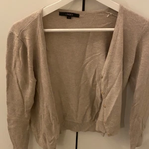 Beige kofta från Lindex - Säljer en klassisk beige kofta från Lindex med långa ärmar och knappar framtill. Perfekt att slänga över en topp eller klänning för en enkel och stilren look.