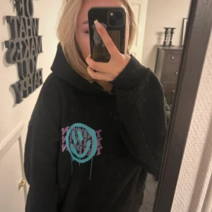 Svart hoodie med tryck - Säljer en svart hoodie med ett coolt tryck i turkos och lila. Perfekt för en avslappnad stil. Hoodien har en stor och bekväm huva.