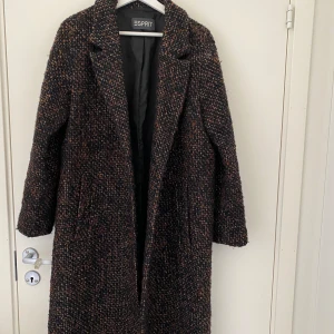 Lång brun kappa - Elegant och tidlös kappa från Esprit i brunt tweed-tyg. Helt oanvänd och av hög kvalitet! Den långa designen gör den perfekt för kyligare dagar, och det stilrena snittet passar både till vardags och finare tillfällen.