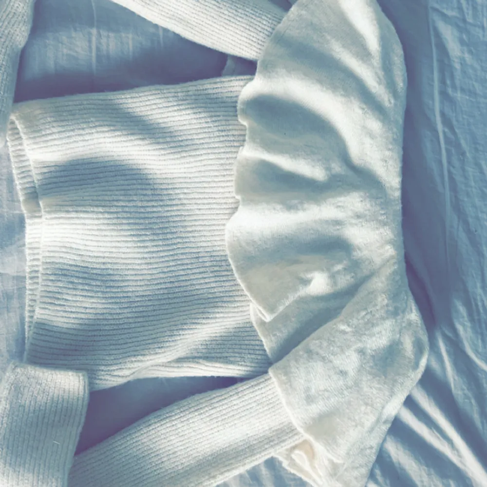 Säljer en stilren vit stickad tröja från H&M. Tröjan har en ribbad struktur och volangdetaljer som ger en unik touch. Perfekt för att hålla sig varm och snygg under kyligare dagar. Passar bra till både jeans och kjol!. Man kan också ha den utomlands eller på sommaren, passar perfekt!. Neuletakit & Villapaidat.